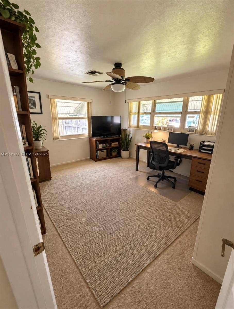 Room featuring neutral wall-to-wall carpeting, abundant natural light from multi-pane windows, and a ceiling-mounted light fixture with a five-blade fan