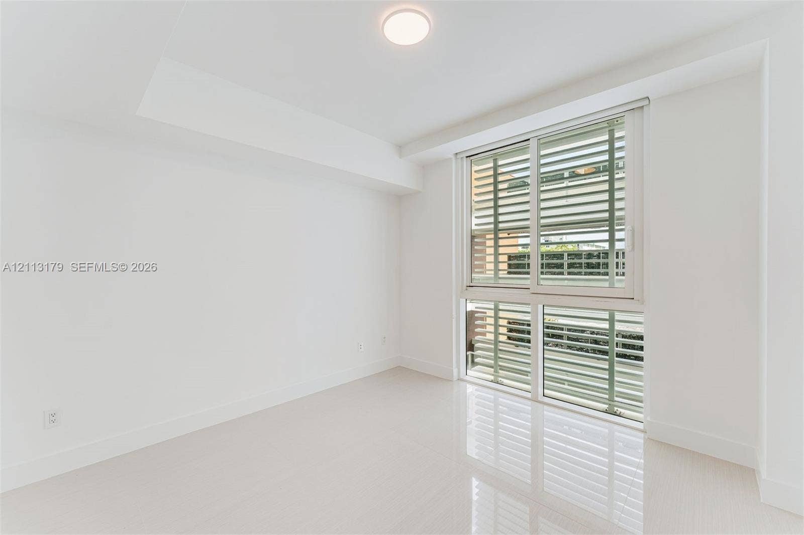 1150 102nd Street, #703, Bay Harbor Islands, FL 33154 Room featuring polished tile flooring, white walls, recessed ceiling lighting, and large sliding windows with exterior horizontal louvers