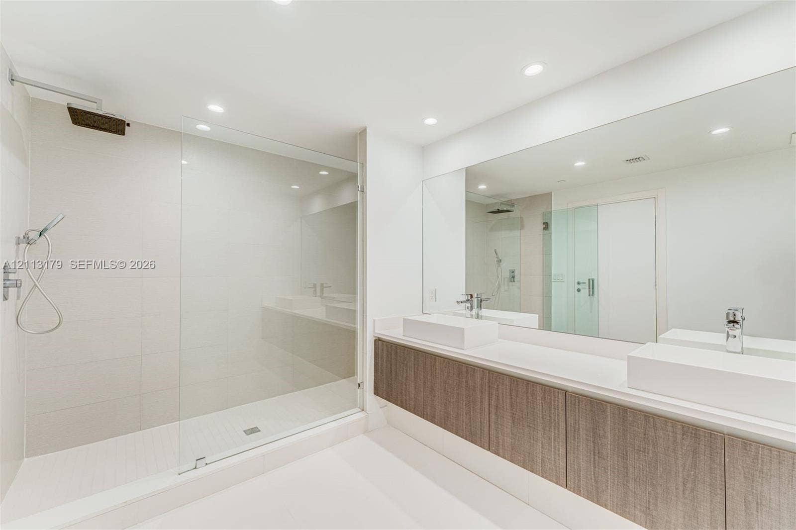 1150 102nd Street, #703, Bay Harbor Islands, FL 33154 Dual vanity featuring rectangular vessel sinks, quartz countertops, wood-finish cabinetry, frameless glass shower enclosure, and ceiling-mounted rainfall showerhead