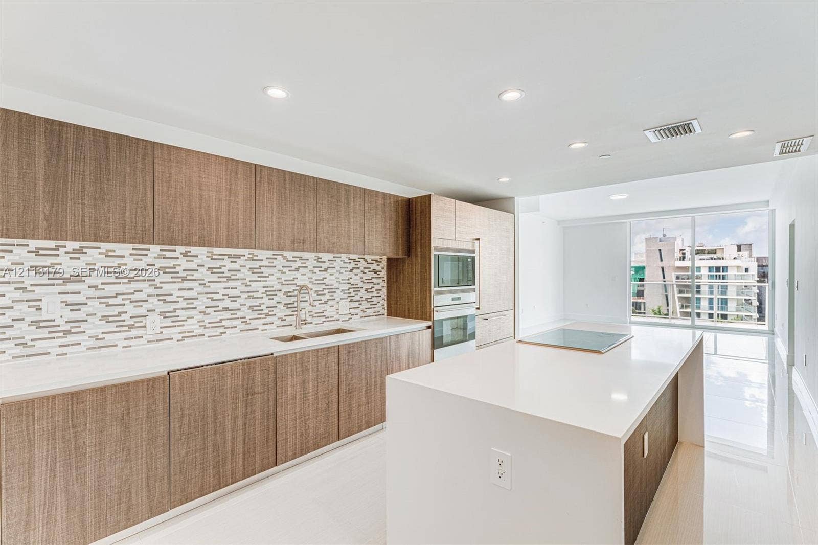 1150 102nd Street, #703, Bay Harbor Islands, FL 33154 Kitchen featuring wood-finish cabinetry, quartz countertops, mosaic tile backsplash, built-in wall oven and microwave, and a large center island with an integrated cooktop