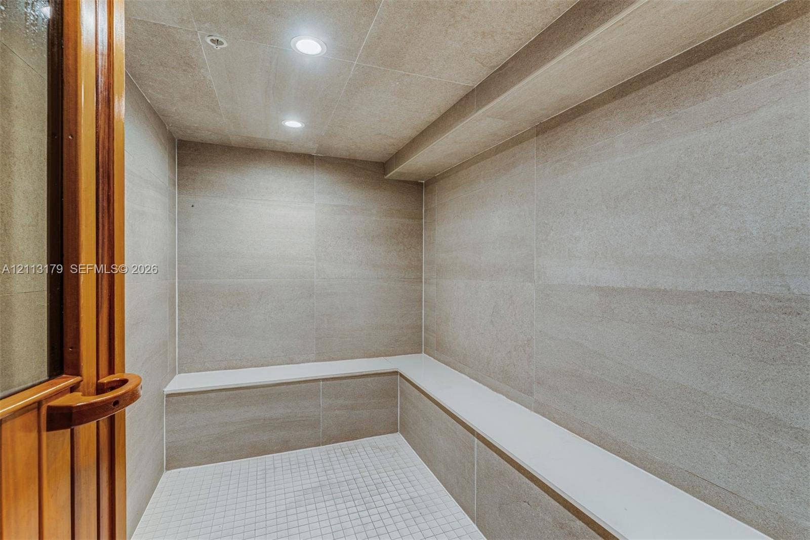 1150 102nd Street, #703, Bay Harbor Islands, FL 33154 Steam room featuring large-format stone-tile walls, built-in tiered stone seating, mosaic-tile flooring, and recessed lighting behind a wood-framed glass door