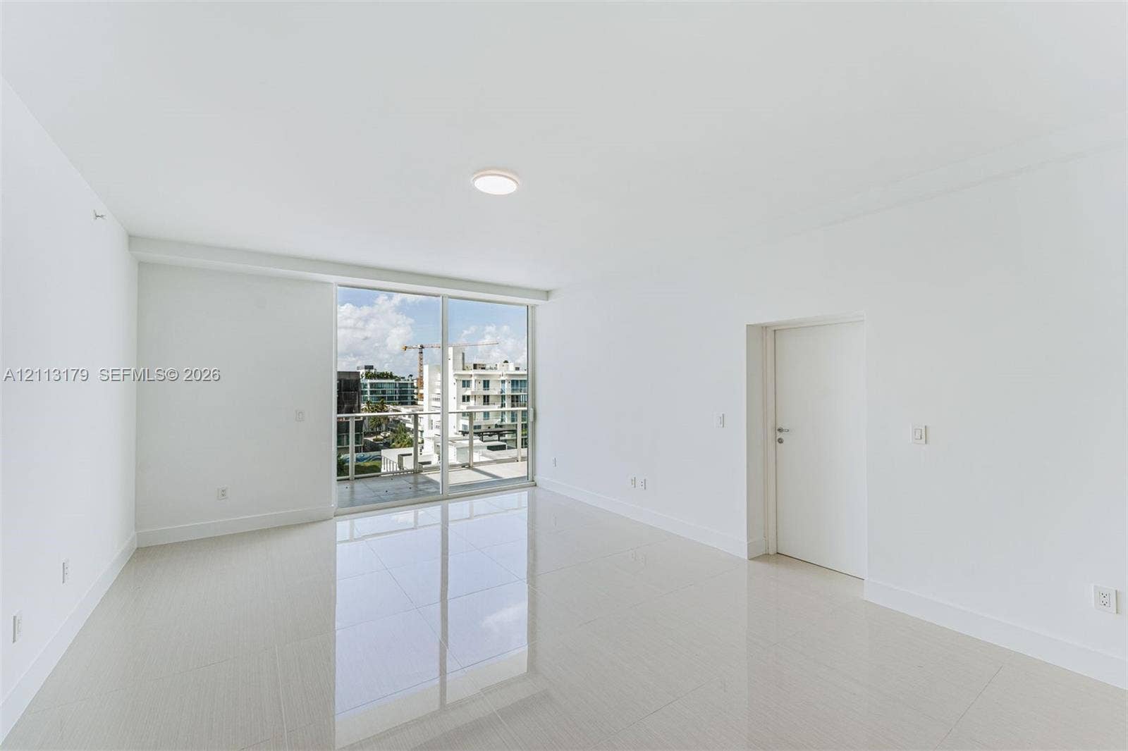 1150 102nd Street, #703, Bay Harbor Islands, FL 33154 Open-concept room featuring light-toned tile flooring, recessed ceiling lighting, and sliding glass doors with access to a glass-railed balcony