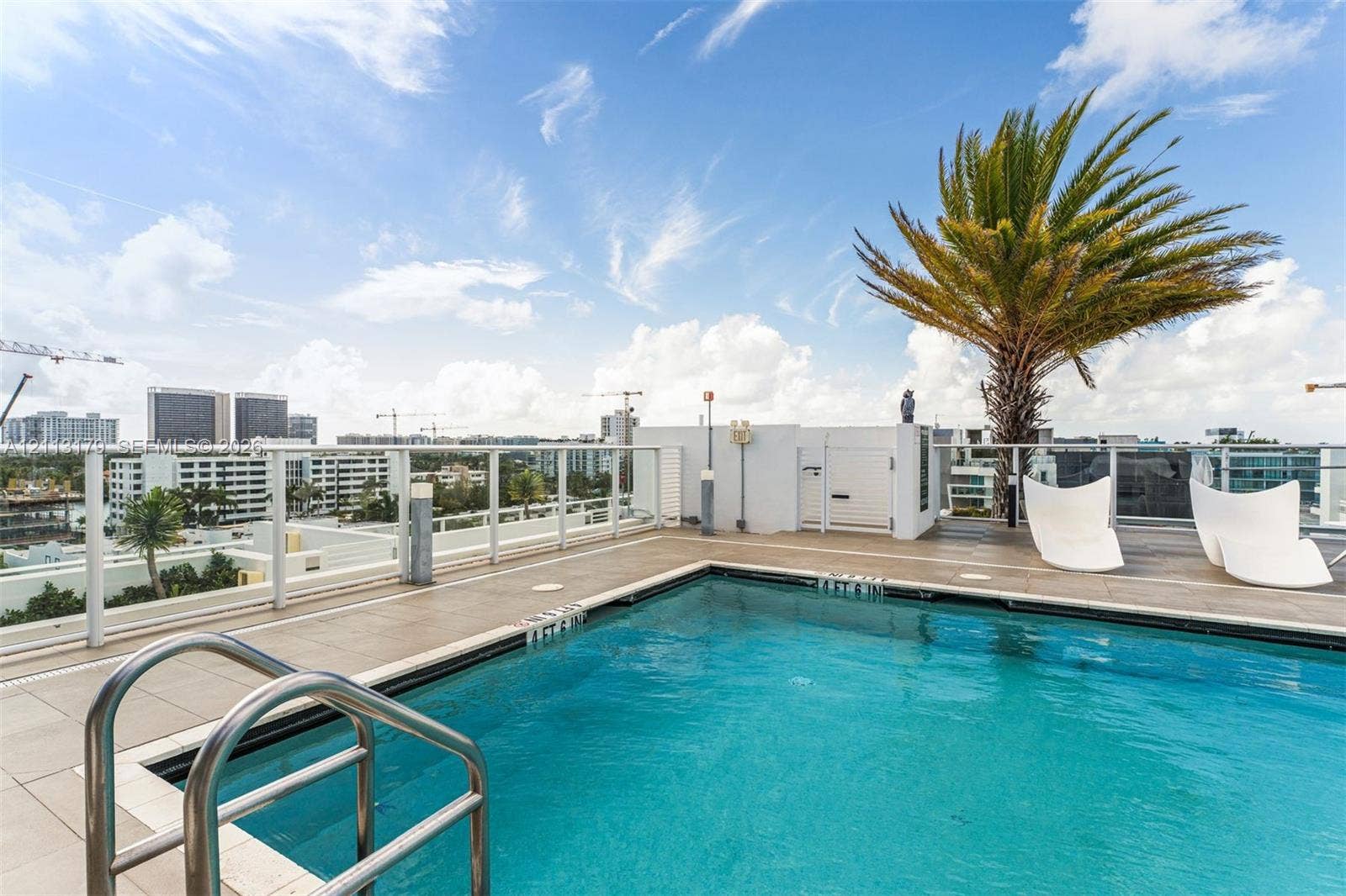 1150 102nd Street, #703, Bay Harbor Islands, FL 33154 Rooftop swimming pool featuring large-format tile decking, glass perimeter railing, and stainless steel ladder