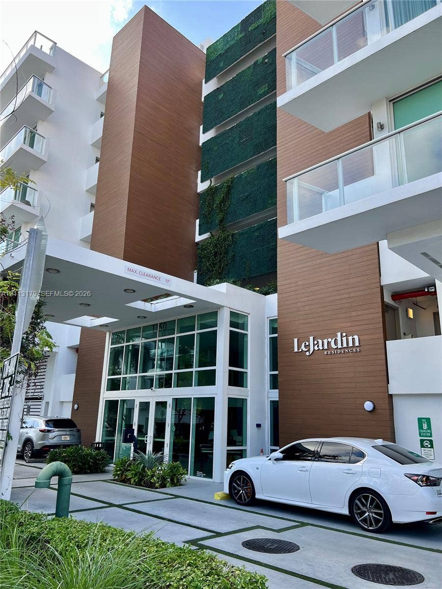 1150 102nd Street, #703, Bay Harbor Islands, FL 33154 Modern building facade featuring wood-finish paneling, vertical green wall detailing, expansive floor-to-ceiling glass entryway, white structural accents, and private balconies with glass railings