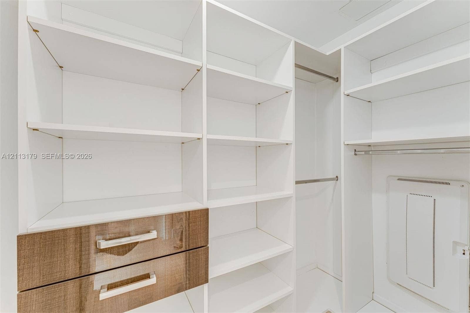1150 102nd Street, #703, Bay Harbor Islands, FL 33154 Custom reach-in closet featuring white adjustable shelving, two integrated drawers with wood-finish fronts, metal hardware, and dual hanging rods