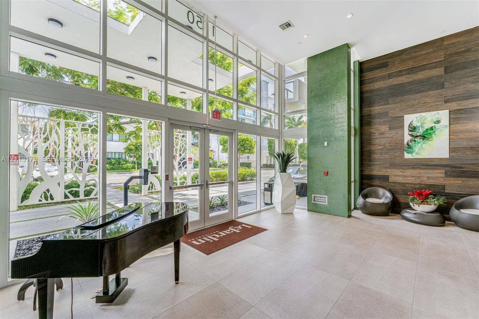 1150 102nd Street, #703, Bay Harbor Islands, FL 33154 Grand entrance lobby featuring double-height glass curtain walls, floor-to-ceiling windows, large-format tile flooring, a vibrant green accent pillar, and horizontal wood-finish wall paneling