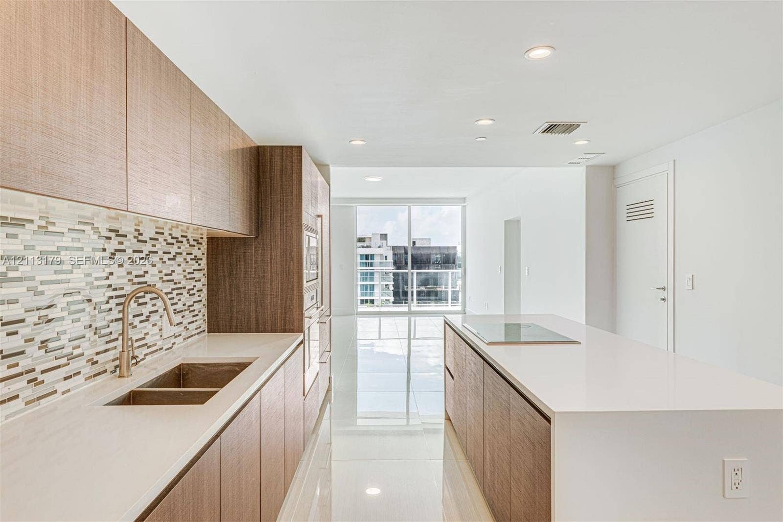 1150 102nd Street, #703, Bay Harbor Islands, FL 33154 Kitchen featuring wood-finish cabinetry, stone-surface countertops, mosaic tile backsplash, integrated stainless steel appliances, and a central island with a flush-mount cooktop