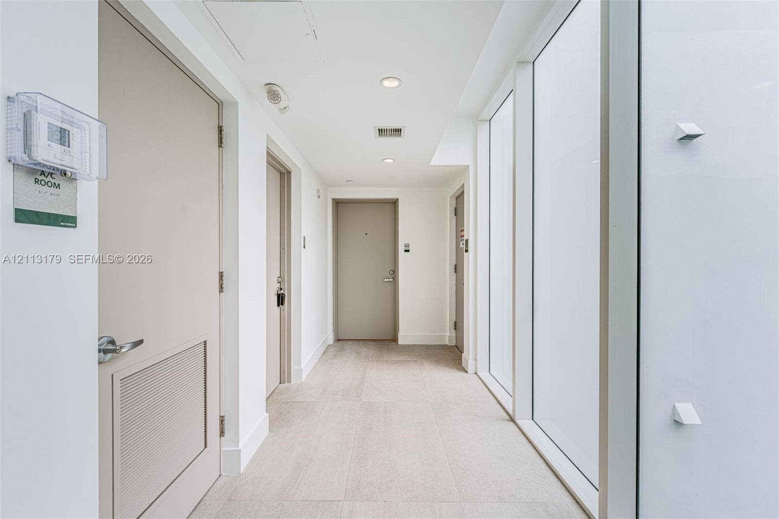 1150 102nd Street, #703, Bay Harbor Islands, FL 33154 Interior corridor featuring large-format tile flooring, floor-to-ceiling glass wall panels, recessed lighting, and solid-core doors
