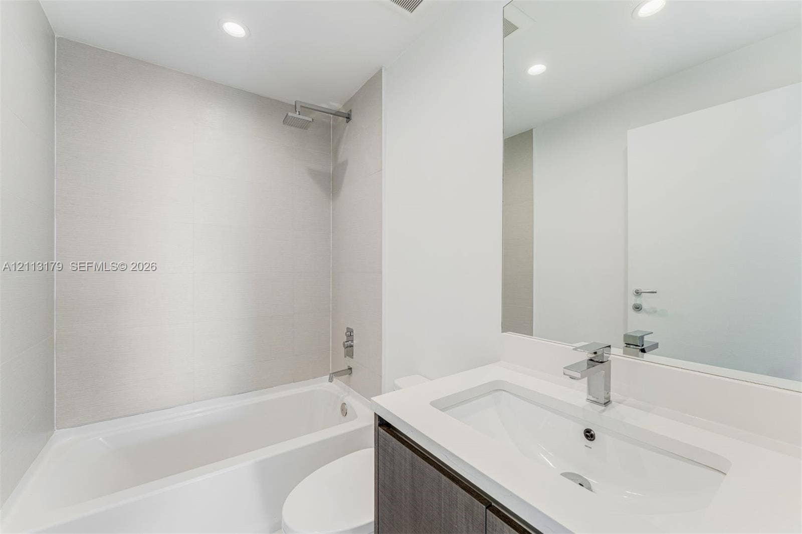 1150 102nd Street, #703, Bay Harbor Islands, FL 33154 Bathroom featuring a large-format tiled shower surround with a rain-style showerhead, a deep soaking tub, and a vanity topped with a rectangular integrated sink and a chrome single-handle faucet