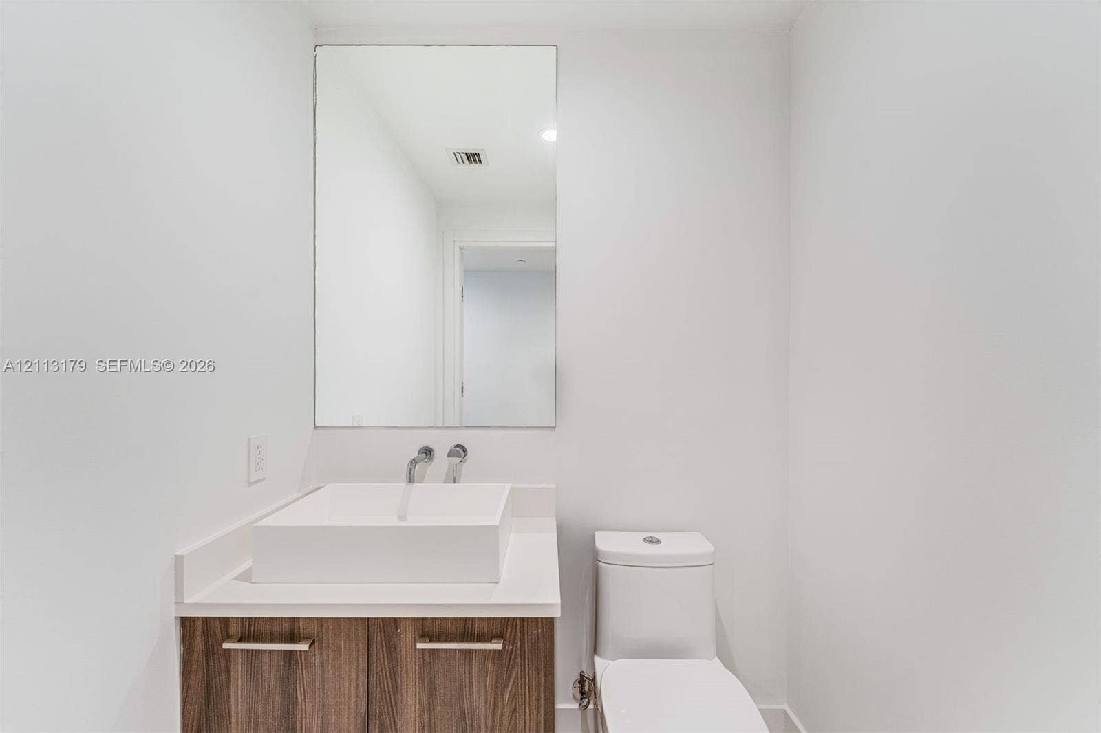 1150 102nd Street, #703, Bay Harbor Islands, FL 33154 Floating wood-finish vanity with a rectangular vessel sink, solid-surface countertop, wall-mounted faucet, and a large frameless mirror