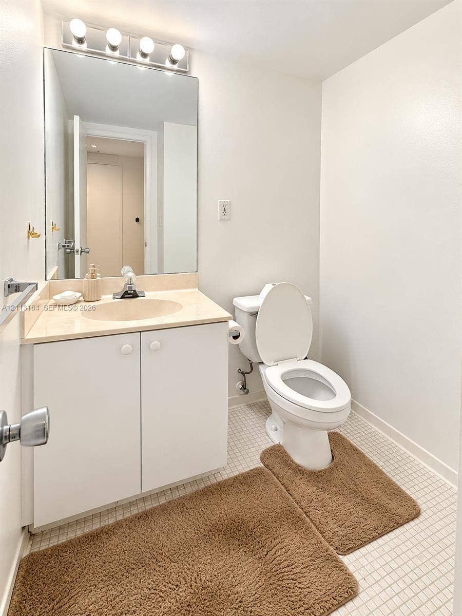 19380 Collins Avenue, #708, Sunny Isles Beach, Sunny Isles Beach, FL 33160 Bathroom featuring a white vanity cabinet, solid-surface countertop with an integrated sink, expansive wall-mounted mirror, four-bulb vanity light fixture, and mosaic tile flooring