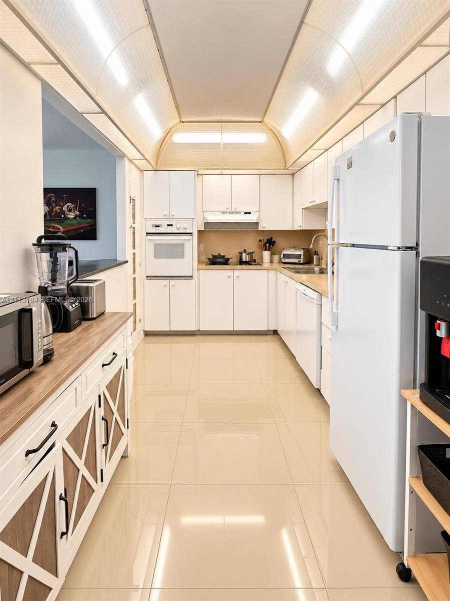 19380 Collins Avenue, #708, Sunny Isles Beach, Sunny Isles Beach, FL 33160 Kitchen featuring a barrel-vaulted ceiling, high-gloss tile flooring, white cabinetry with integrated appliances, and a wood-finish countertop