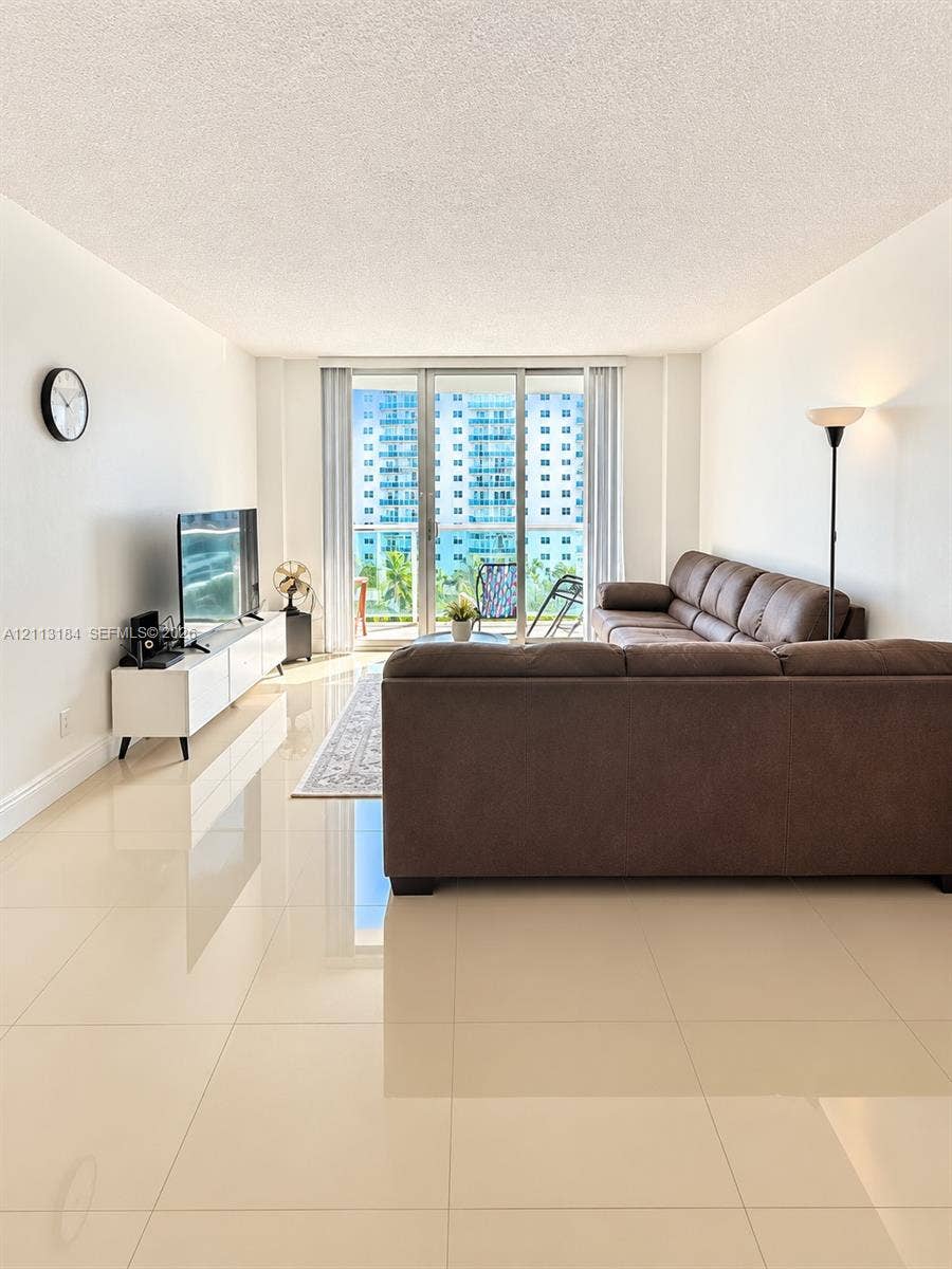 19380 Collins Avenue, #708, Sunny Isles Beach, Sunny Isles Beach, FL 33160 Living area featuring polished large-format tile flooring and floor-to-ceiling glass sliding doors opening to a balcony