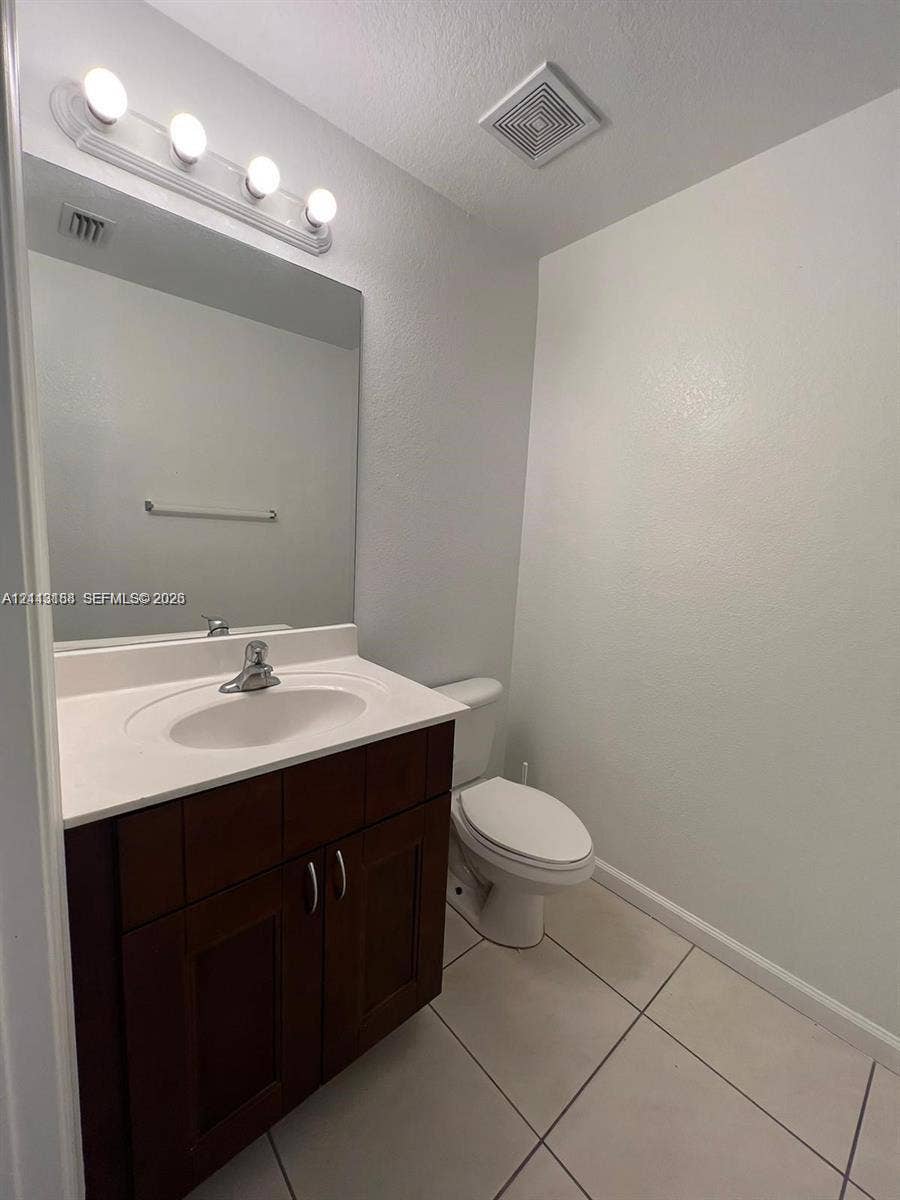 8706 NW 38th Drive, #2, Coral Springs, Coral Springs, FL 33065 Dark wood-finish vanity with a white countertop, integrated sink, polished chrome faucet, and large wall-mounted vanity mirror with multi-bulb light fixture, complemented by tile flooring