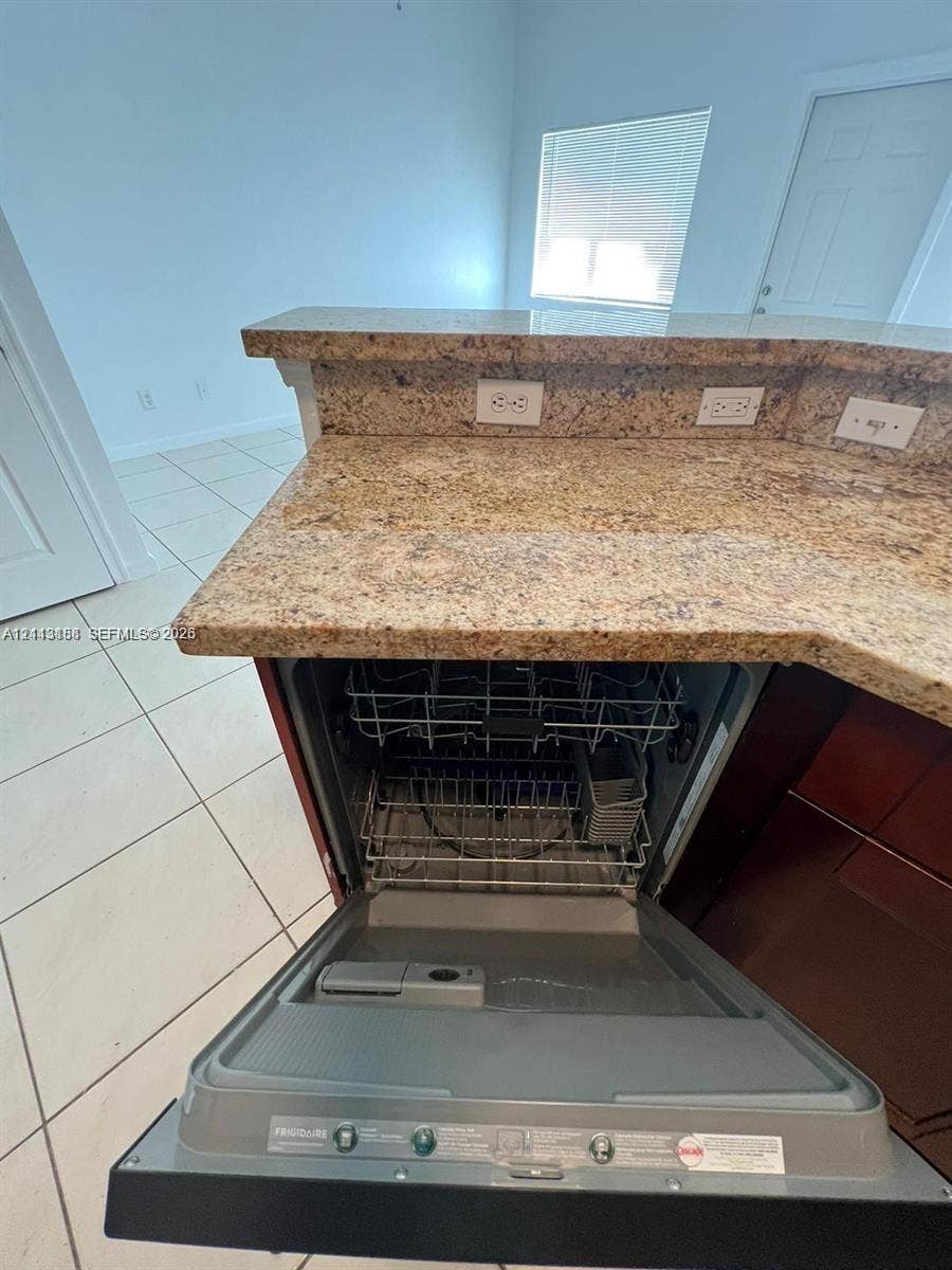 8706 NW 38th Drive, #2, Coral Springs, Coral Springs, FL 33065 Kitchen area featuring stone-surfaced countertops, a breakfast bar, ceramic tile flooring, and an integrated Frigidaire dishwasher