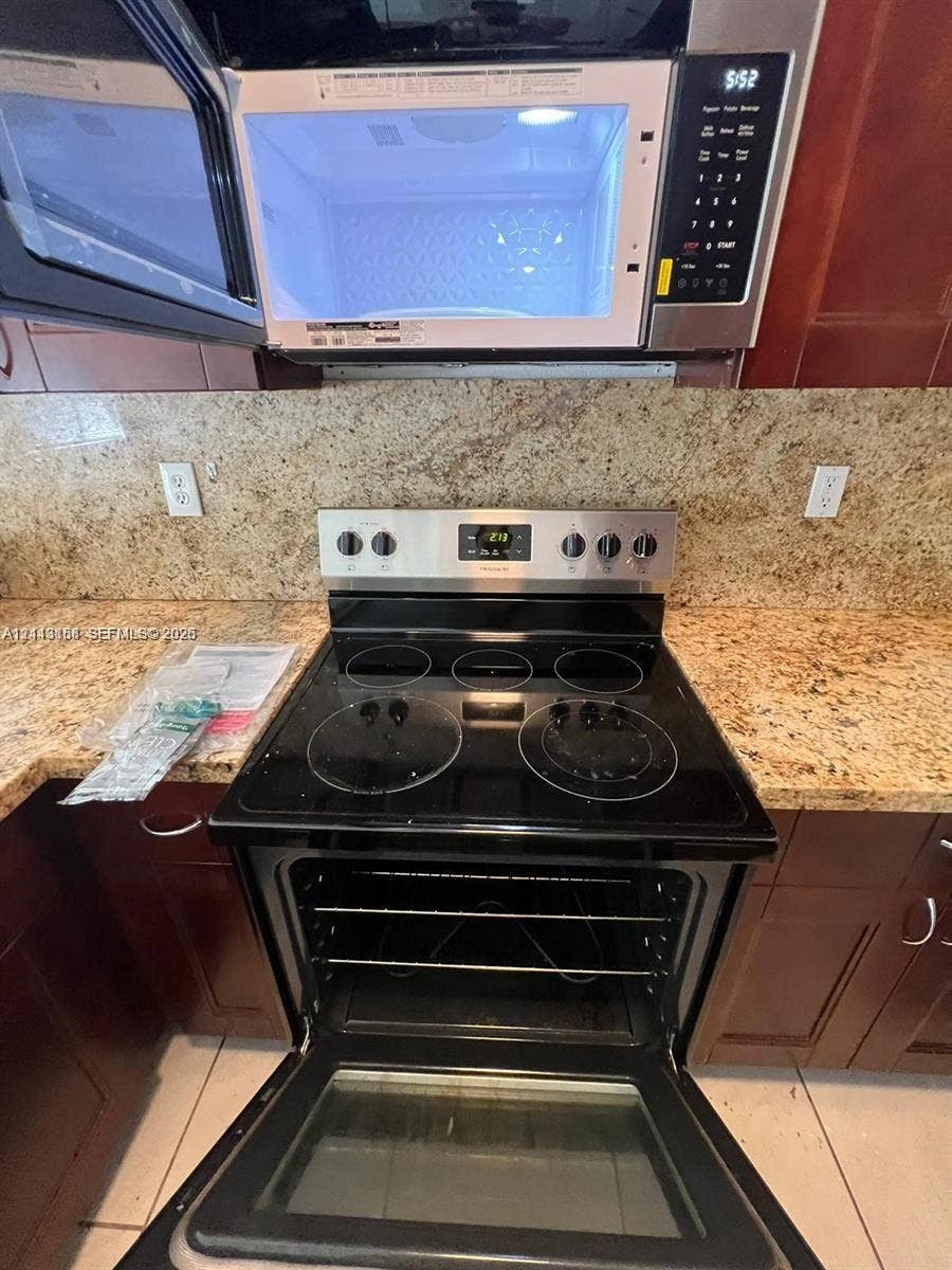 8706 NW 38th Drive, #2, Coral Springs, Coral Springs, FL 33065 Stainless steel electric range with a glass cooktop and matching over-the-range microwave, set against stone-surface countertops and dark wood-finish cabinetry