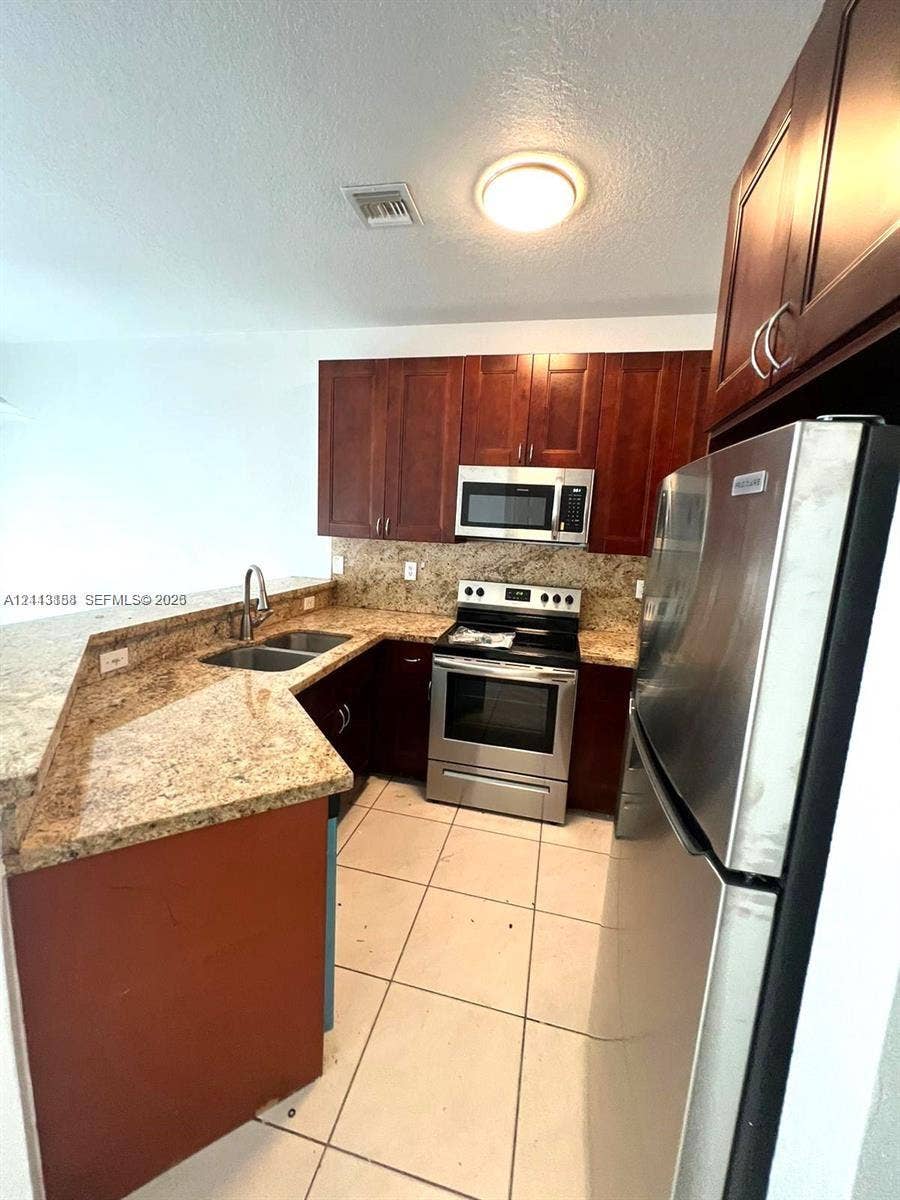 8706 NW 38th Drive, #2, Coral Springs, Coral Springs, FL 33065 Kitchen featuring dark wood cabinetry, stone-surface countertops, dual-basin stainless steel sink, stainless steel kitchen appliances, and tile flooring