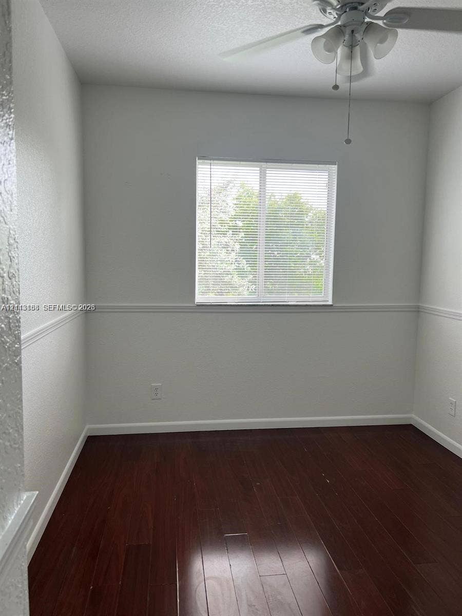 8706 NW 38th Drive, #2, Coral Springs, Coral Springs, FL 33065 Room interior featuring wood-finish flooring, a ceiling fan with integrated lighting, a single-pane sliding window, and chair rail molding
