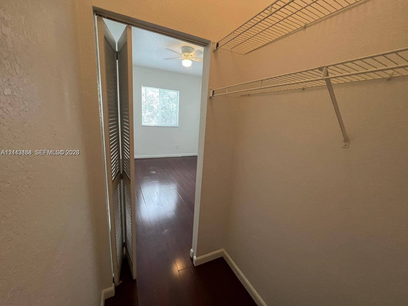 8706 NW 38th Drive, #2, Coral Springs, Coral Springs, FL 33065 Closet featuring white wire shelving and bi-fold louvered doors, with wood-finish flooring, ceiling fan, and window visible in the background