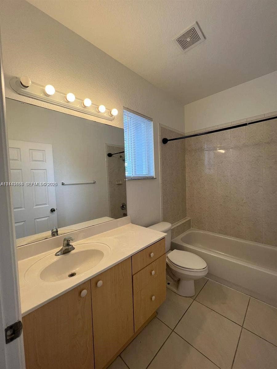 8706 NW 38th Drive, #2, Coral Springs, Coral Springs, FL 33065 Bathroom featuring a vanity with light-wood cabinetry, white solid-surface countertop, integrated basin, wall-mounted mirror, and tile flooring
