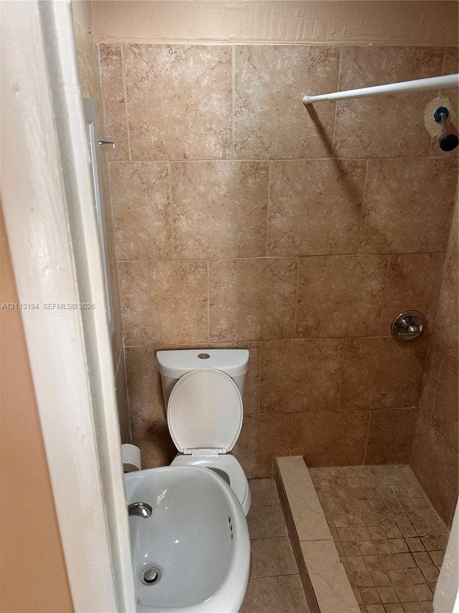 Full-height wall tile, tiled shower surround, integrated shower floor, porcelain toilet, and wall-mounted sink