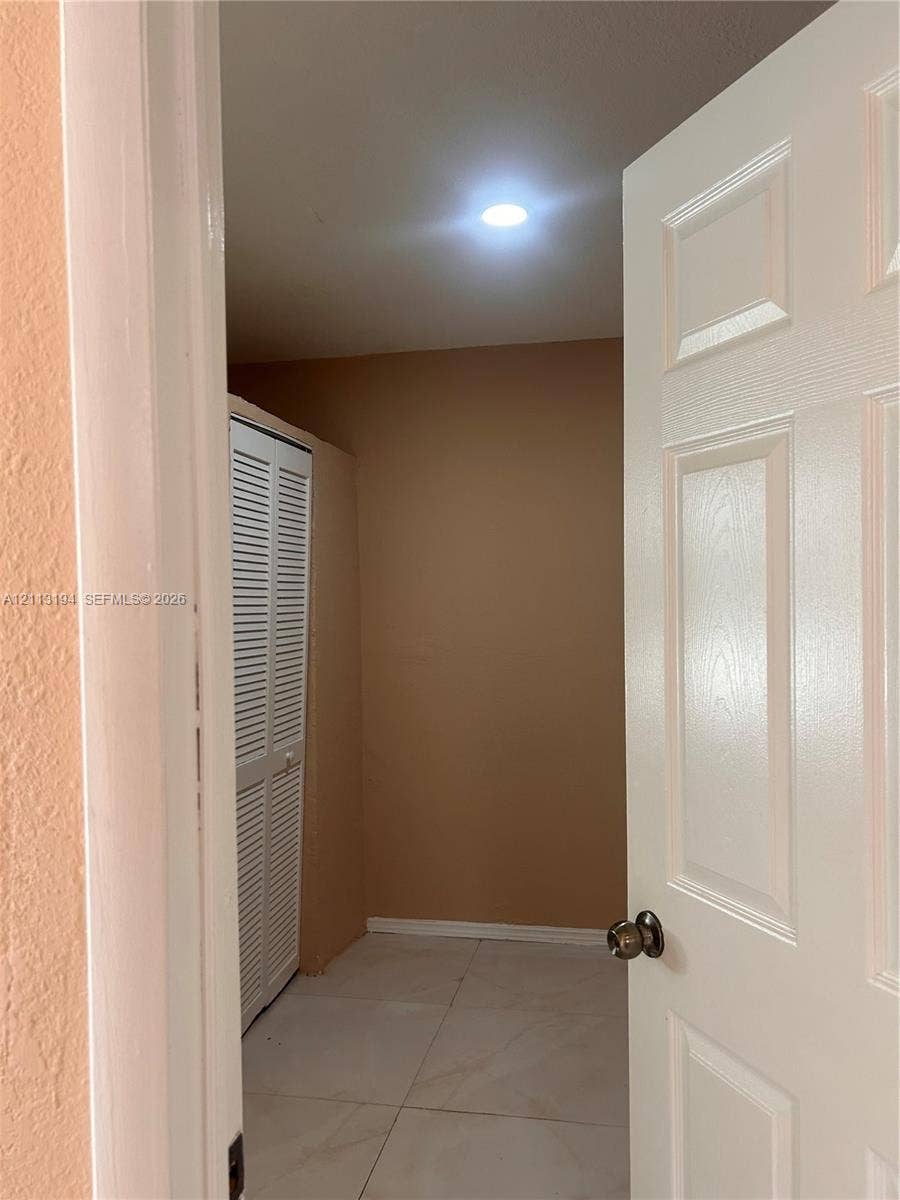 Interior space featuring large-format tile flooring, recessed ceiling lighting, and white louvered-panel closet doors