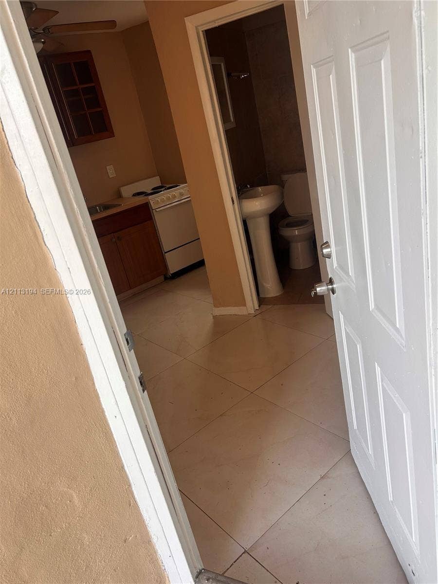 Interior space featuring large-format ceramic floor tiling, wood-finish cabinetry, a white freestanding range, and a pedestal sink