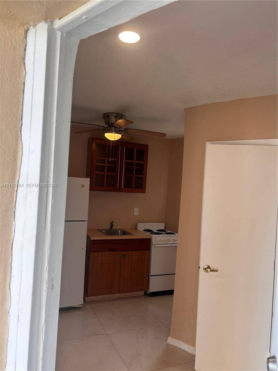 Kitchen featuring wood-finish cabinetry with glass-paneled upper doors, tile flooring, and integrated appliances