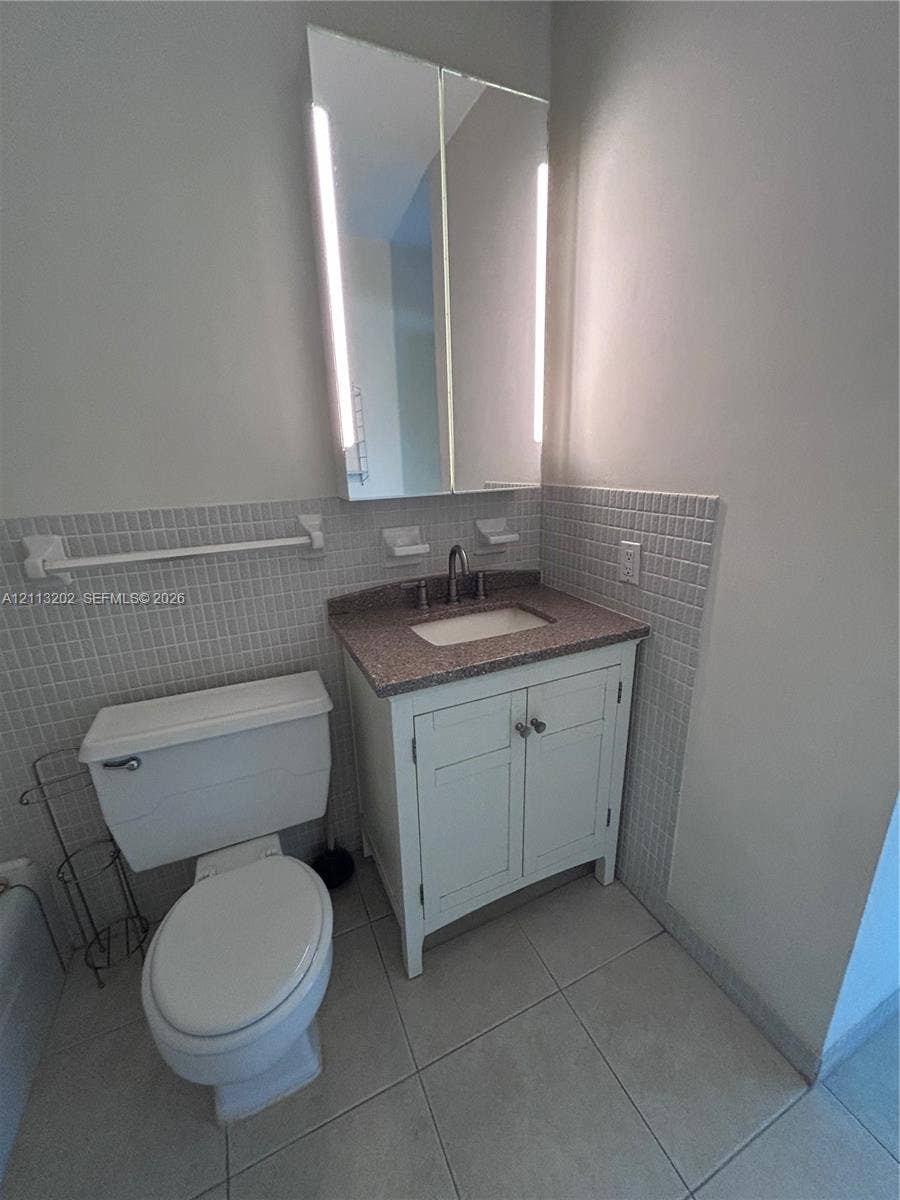 5700 NE 22nd Way, #324, Fort Lauderdale, Fort Lauderdale, FL 33308 Bathroom featuring a vanity with stone-finish countertop, under-mount sink, white cabinetry, integrated medicine cabinet with built-in vertical lighting, and tiled wall surround