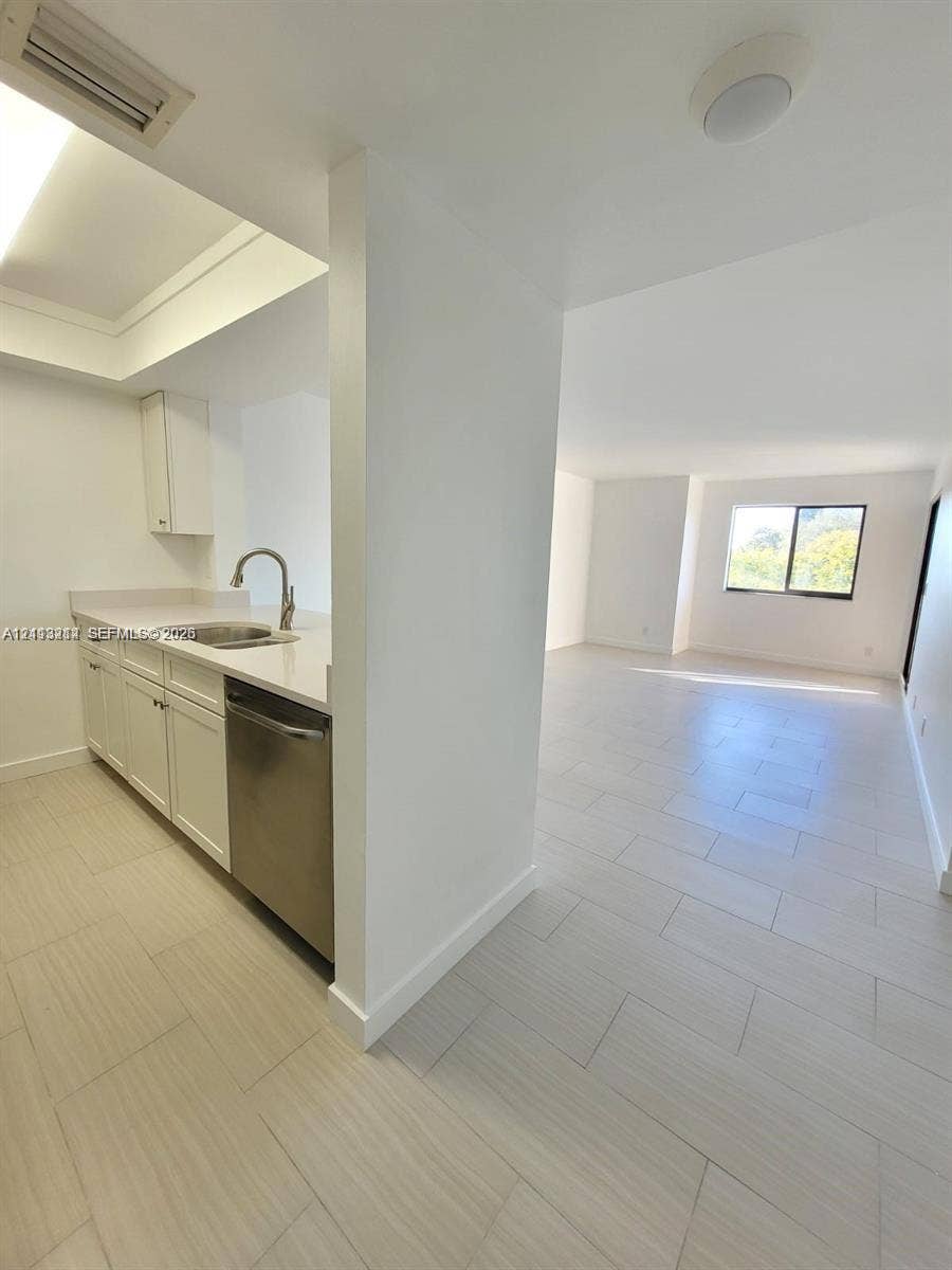 Kitchen featuring white cabinetry, solid-surface countertops, a stainless steel dishwasher, and a circular undermount sink