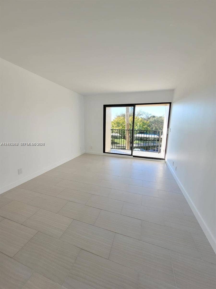 Interior space featuring neutral wall-to-wall tile flooring, minimalist white walls, and a glass sliding door providing access to an exterior balcony