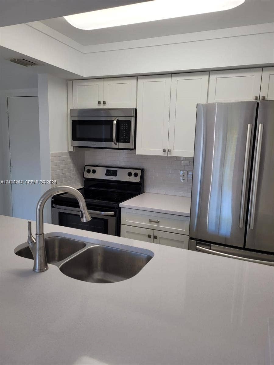 Kitchen featuring white cabinetry, solid-surface countertops, subway tile backsplash, stainless steel appliances, and a double-basin sink with a pull-down faucet