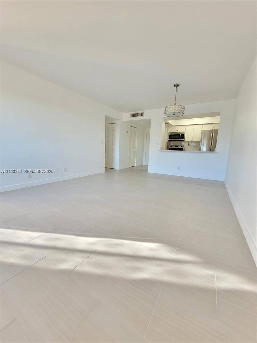 Open living area featuring neutral-tone ceramic tile flooring, a pass-through kitchen opening, drum-style pendant lighting, and crisp white wall finishes