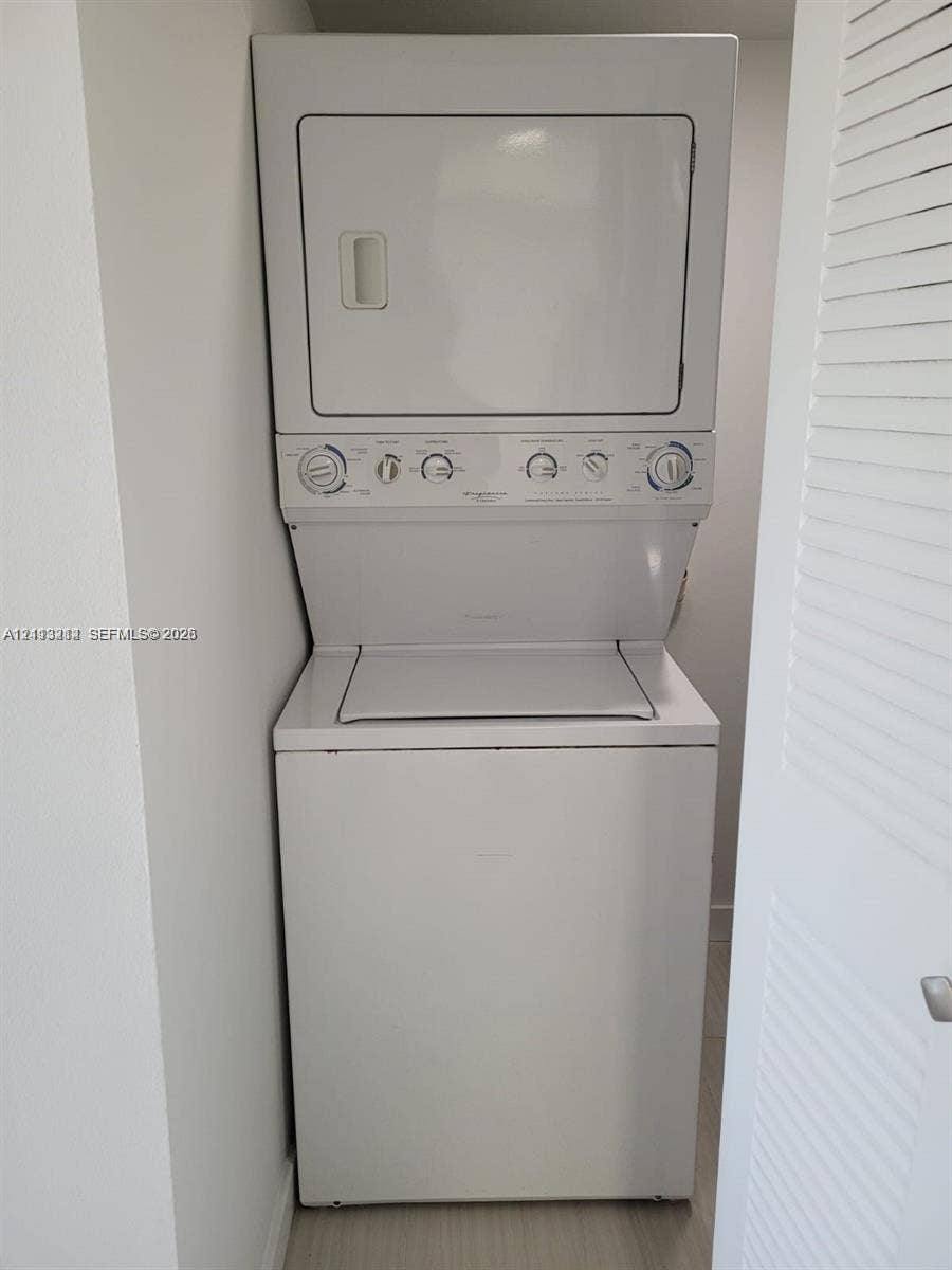 Stacked white washer and dryer unit enclosed within a closet with a louvered door