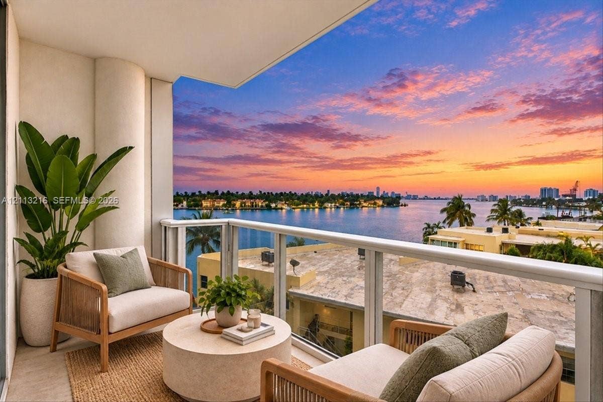 900 Bay Drive, #425, Miami Beach, FL 33141 Covered balcony featuring neutral stone flooring and a glass-paneled railing with a waterfront backdrop