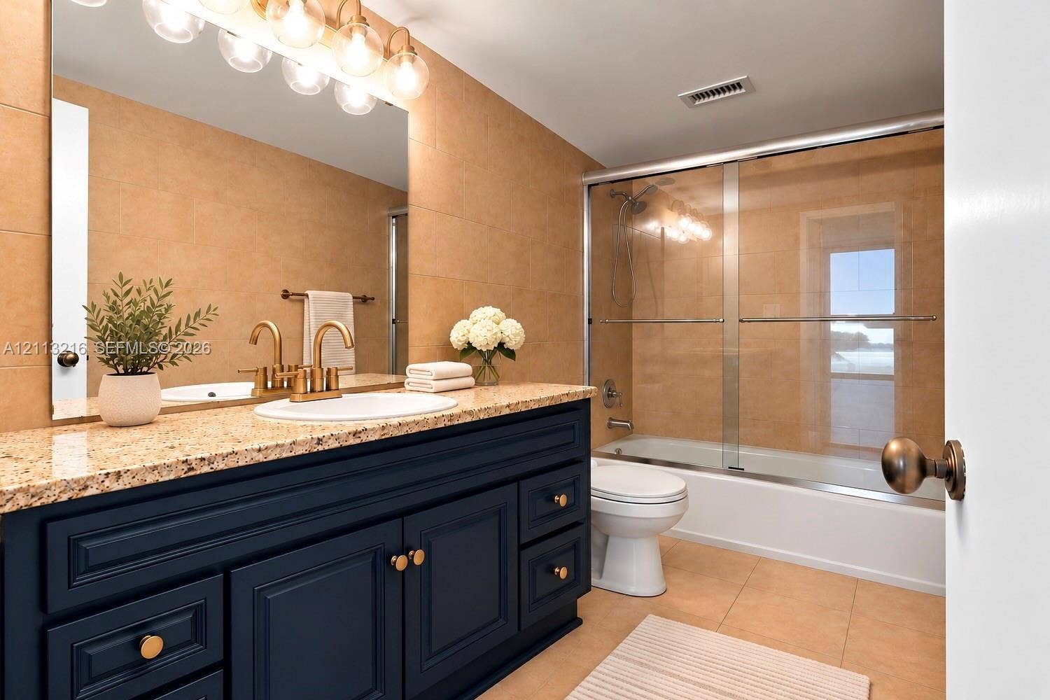 900 Bay Drive, #425, Miami Beach, FL 33141 Bathroom featuring a navy blue vanity with stone countertop, undermount sink, brass-tone hardware, and a glass-enclosed shower and tub combination