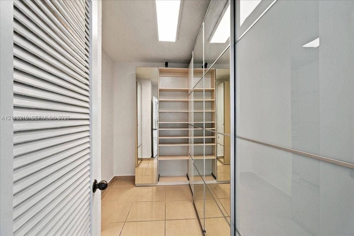 900 Bay Drive, #425, Miami Beach, FL 33141 Storage area featuring built-in wooden shelving, full-height mirrored wardrobe doors, tile flooring, and louvered entry door