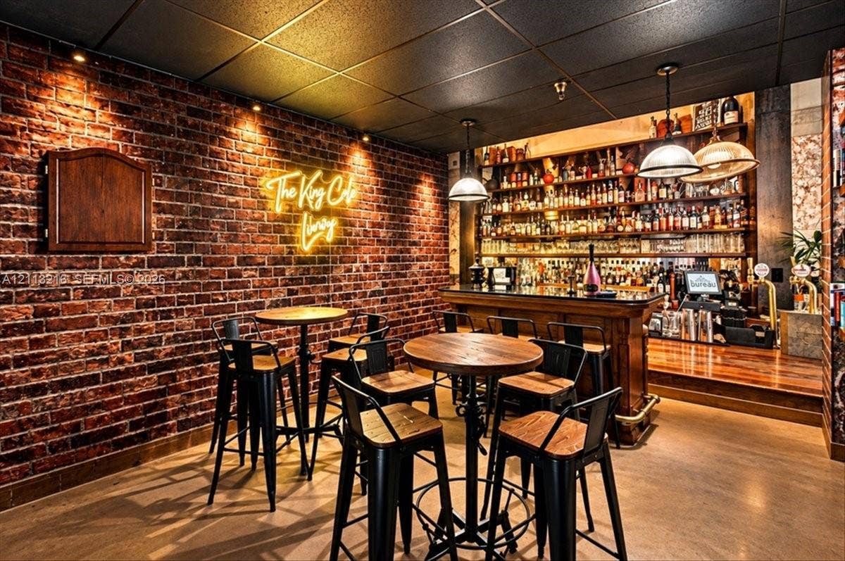900 Bay Drive, #425, Miami Beach, FL 33141 Exposed brick wall with recessed accent lighting, built-in wooden bar, multi-tiered shelving, and dual industrial-style pendant light fixtures