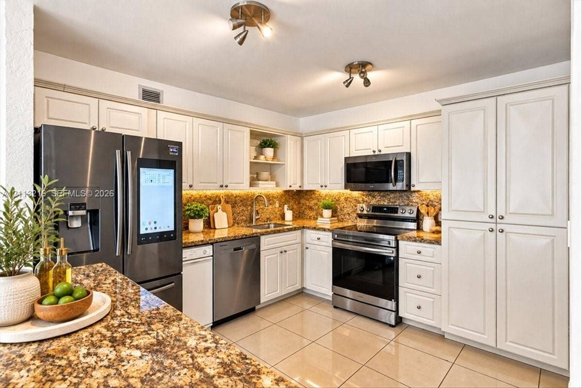 900 Bay Drive, #425, Miami Beach, FL 33141 Kitchen featuring white cabinetry, stone countertops, integrated under-cabinet lighting, tile flooring, and stainless steel appliances