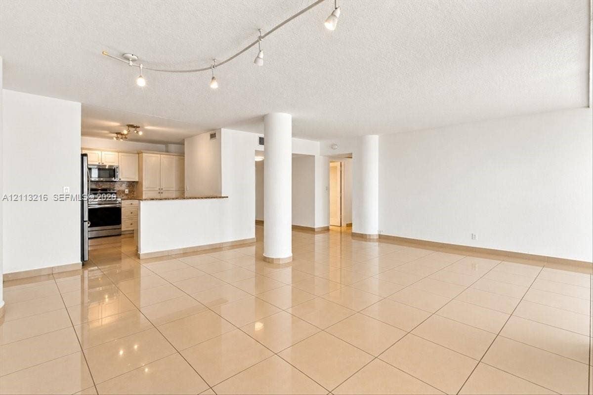 900 Bay Drive, #425, Miami Beach, FL 33141 Open-concept living space featuring high-gloss tile flooring, structural columns, track lighting, and a kitchen with stone-finish countertops and cabinetry