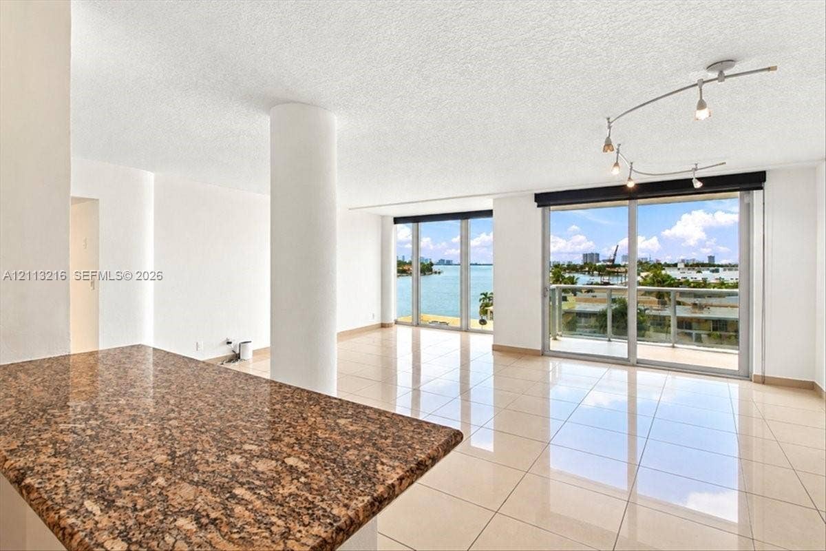 900 Bay Drive, #425, Miami Beach, FL 33141 Open-concept interior featuring large-format tile flooring, a stone-surface breakfast bar, structural pillar, adjustable track lighting, and floor-to-ceiling glass sliding doors opening to an exterior balcony