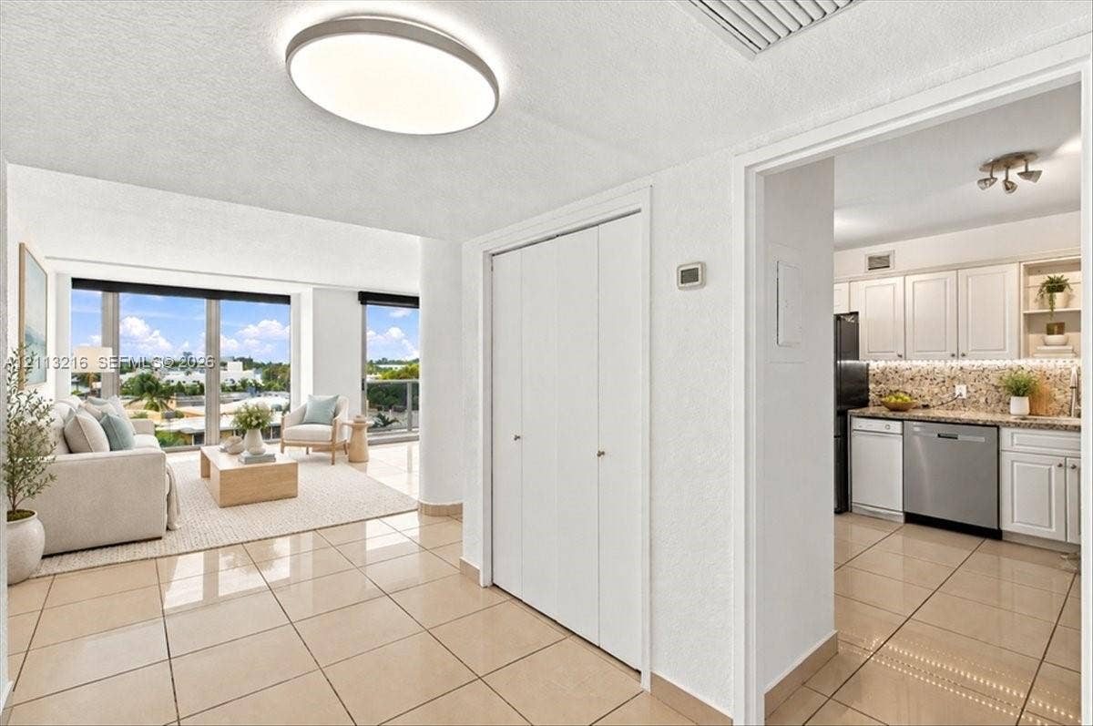900 Bay Drive, #425, Miami Beach, FL 33141 Neutral-toned tile flooring, floor-to-ceiling windows, built-in dual-door closet, and kitchen featuring white cabinetry with stainless steel appliances