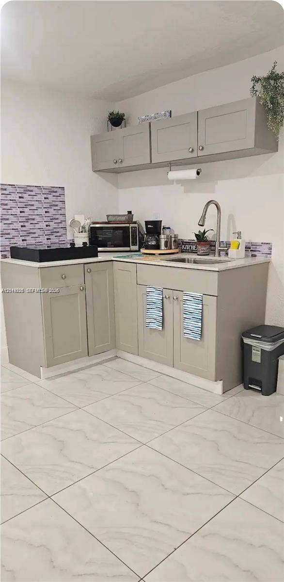 144 NW 7th Avenue, #2, Dania, Dania Beach, FL 33004 Kitchenette featuring neutral-toned cabinetry, light-colored countertops, a single-basin stainless steel sink with a high-arch faucet, patterned wall tiling, and large-format floor tiling