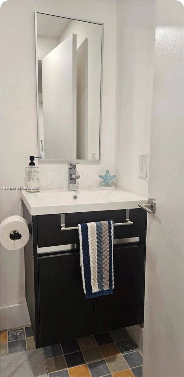 144 NW 7th Avenue, #2, Dania, Dania Beach, FL 33004 Dark-toned vanity with a rectangular sink, polished chrome faucet, rectangular wall-mounted mirror, and multi-colored square tile flooring