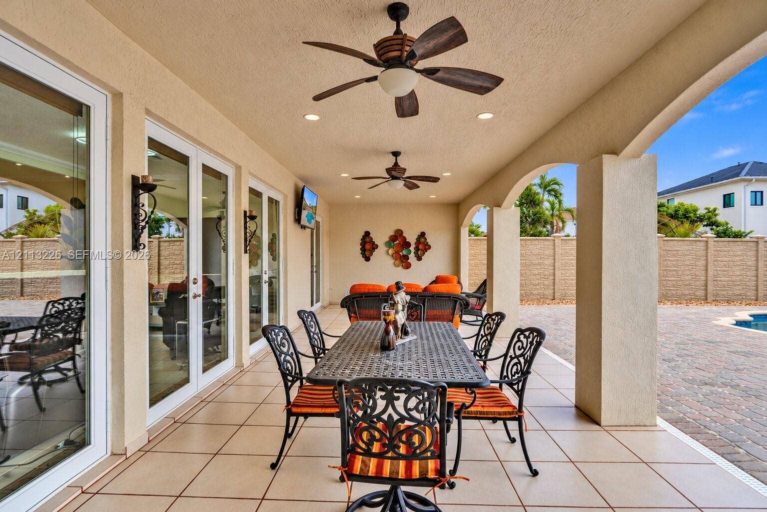 Covered patio featuring tiled flooring, recessed lighting, dual ceiling fans, arched support columns, and multi-panel sliding glass doors