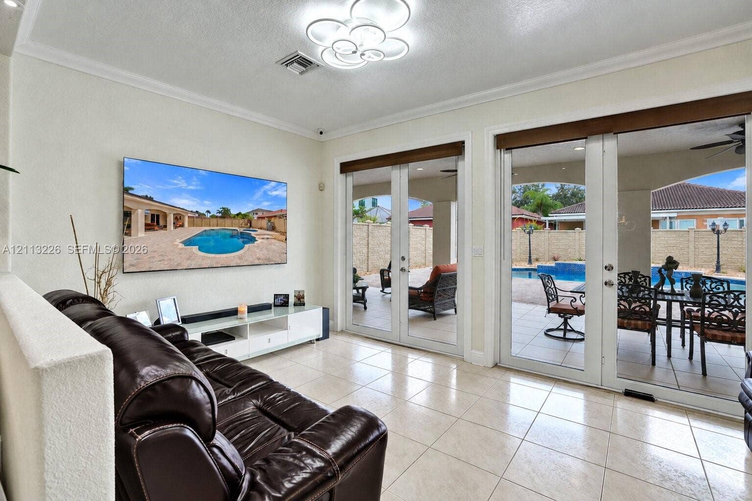 Neutral tile flooring, multi-light contemporary ceiling fixture, and dual sets of glass-paned double doors providing outdoor access