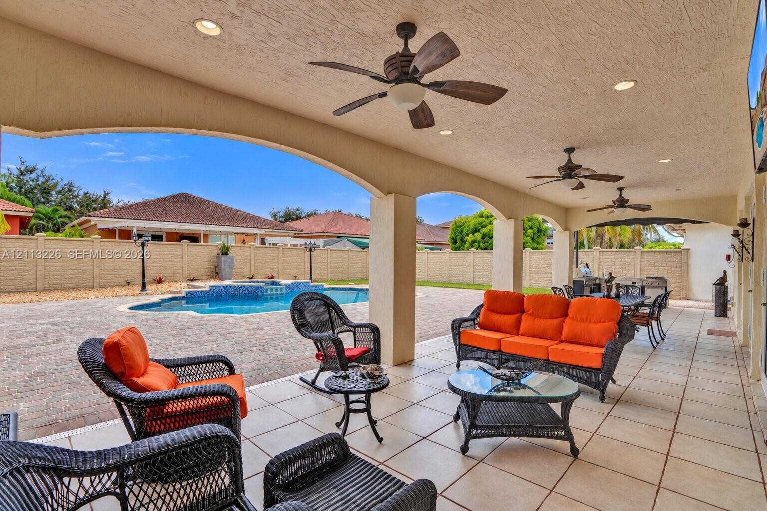 Covered lanai featuring a tile floor, arched structural supports, recessed lighting, and ceiling fans, with an outdoor pool and paved patio area