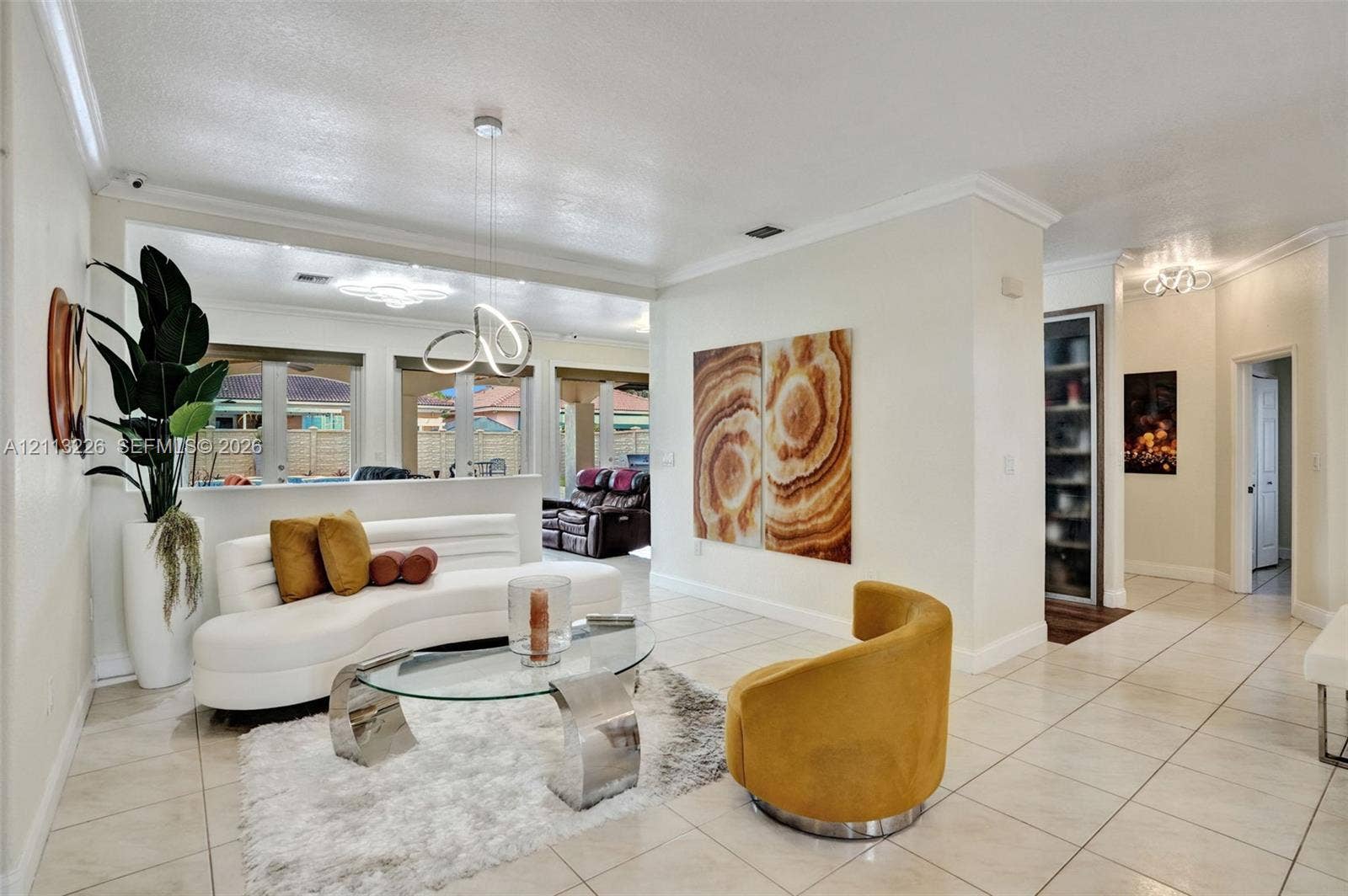 Open-concept living space featuring large-format tile flooring, crown molding, modern sculptural pendant lighting, and multiple French door entries