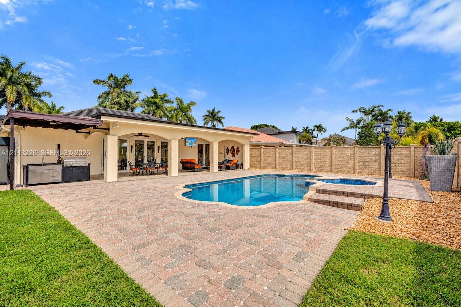 Covered patio with integrated outdoor kitchen, stone paver decking, swimming pool, and attached spa enclosed by a privacy wall