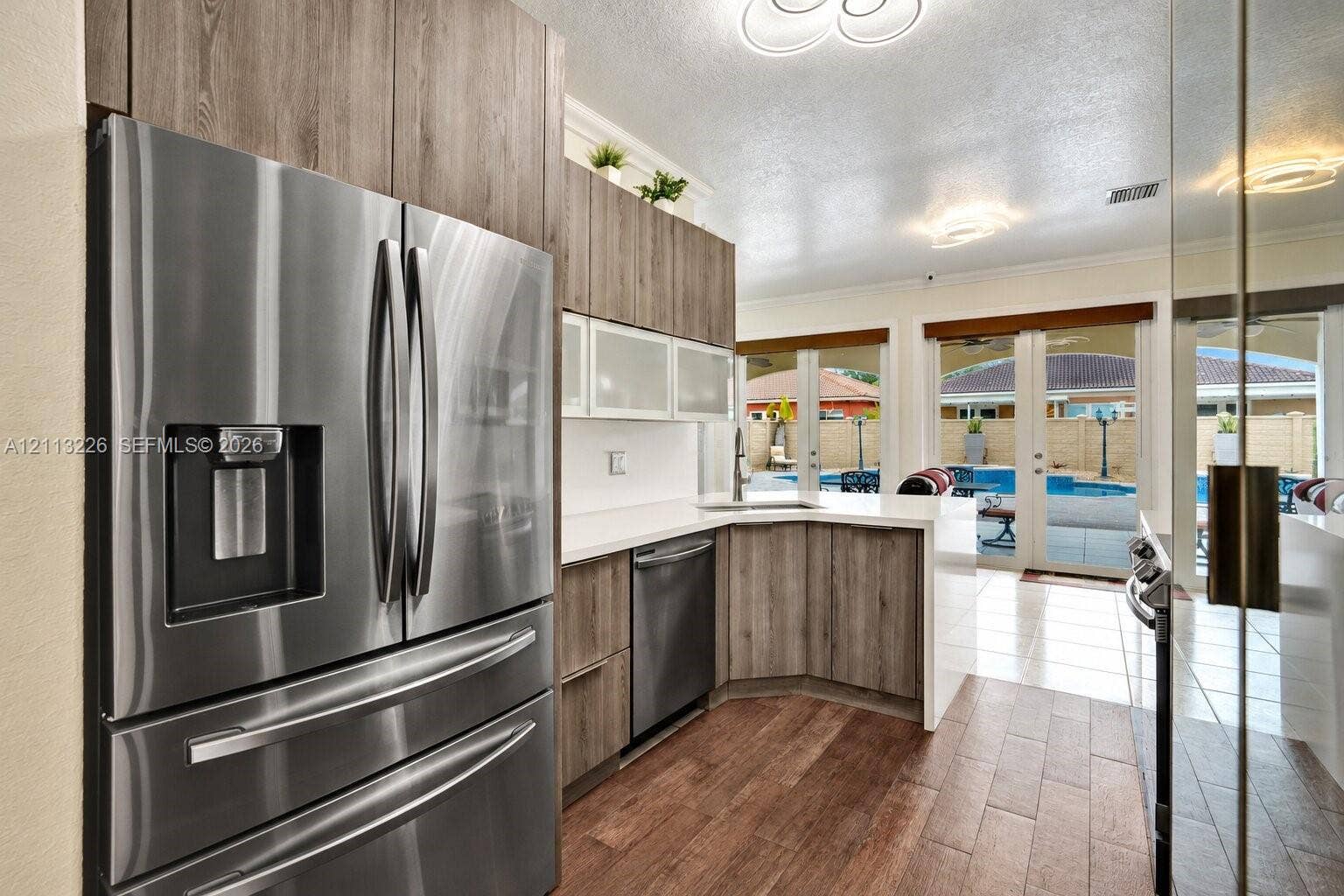 Kitchen featuring flat-panel wood-finish cabinetry, stainless steel appliances, solid-surface countertops, tile flooring, and multiple glass-paned double doors